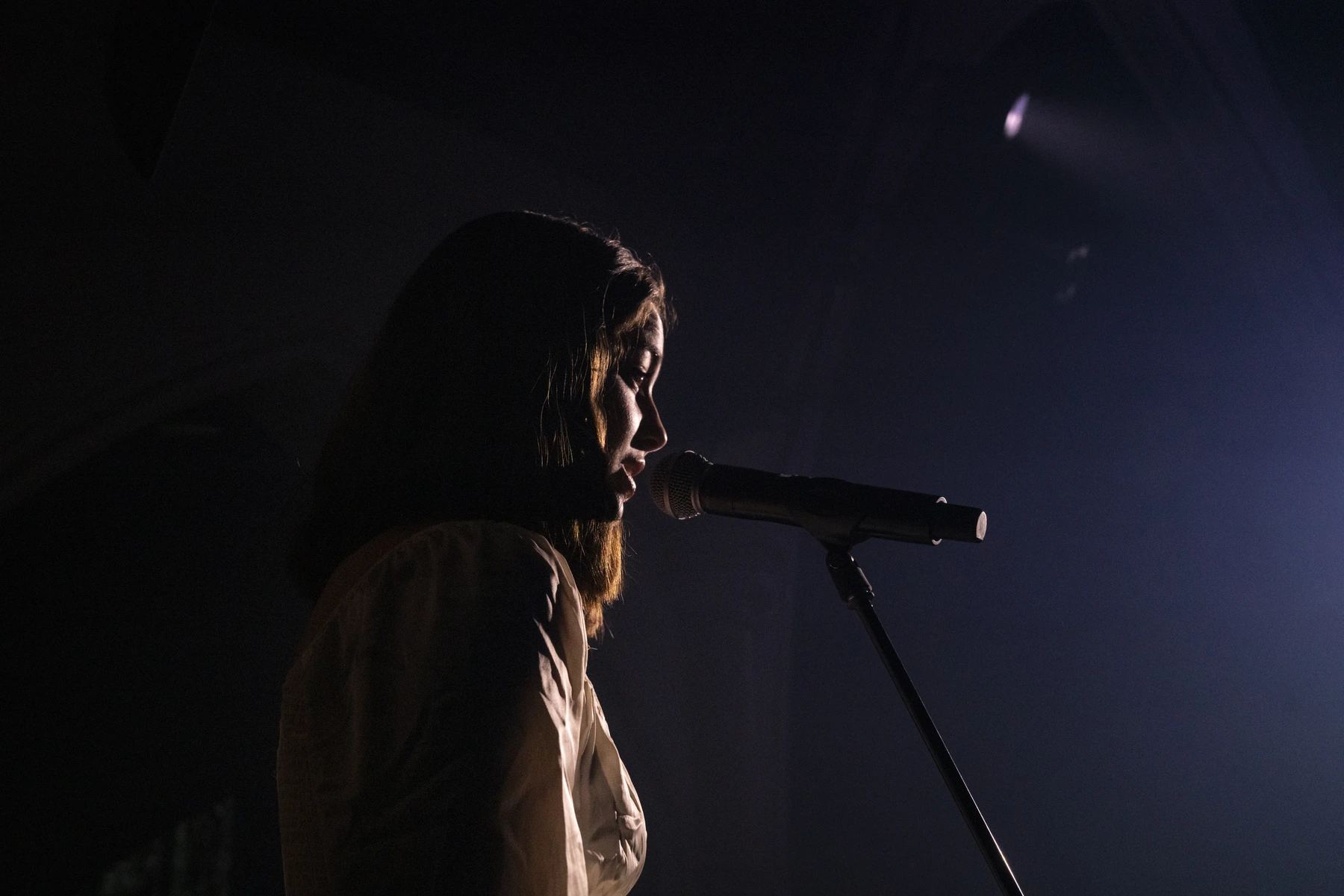 Une interprète chante au micro, son profil éclairé dans la pénombre.