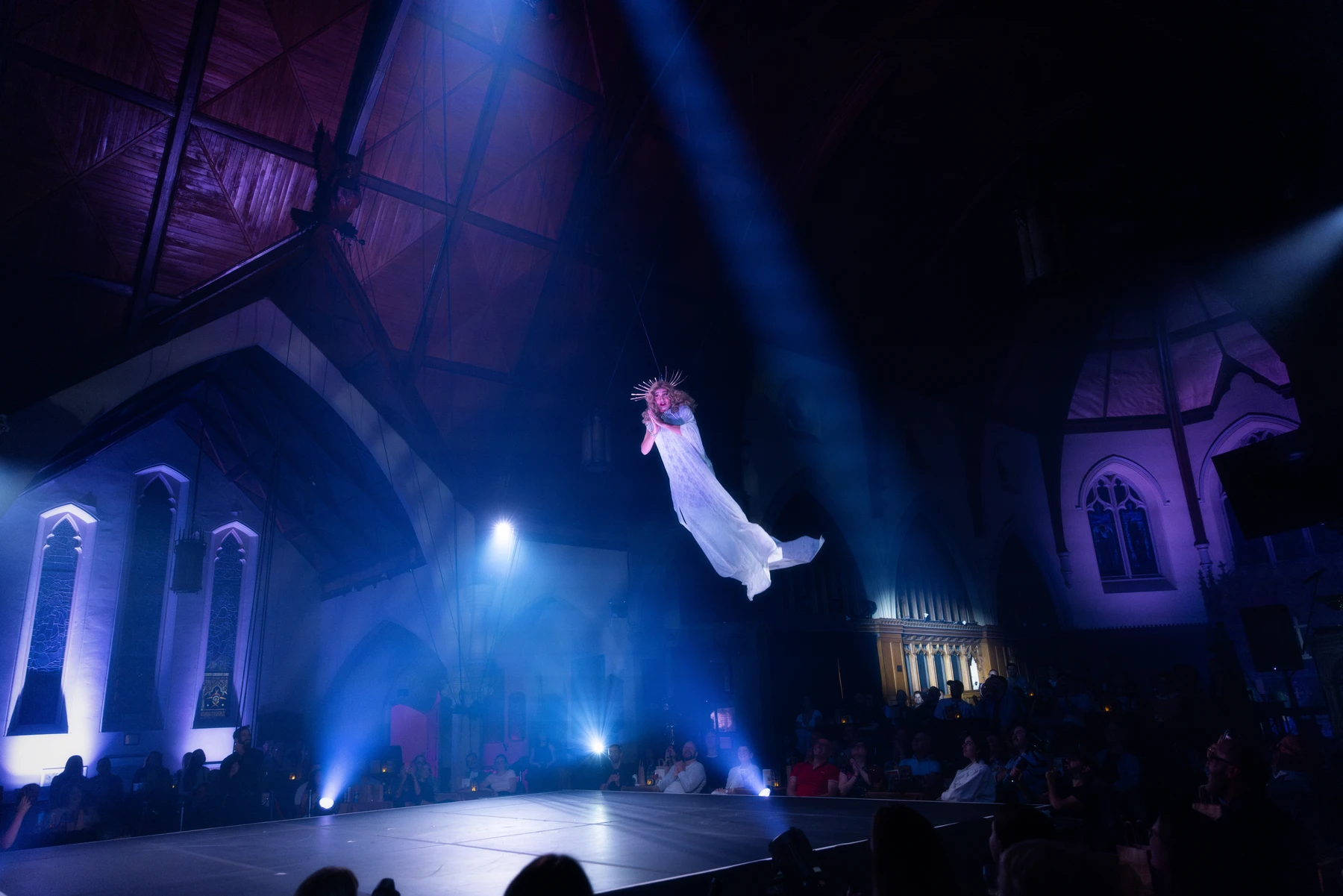 Une figure en robe blanche suspendue dans la salle du spectacle Envol, photographiée par Harmony Le Reste.
